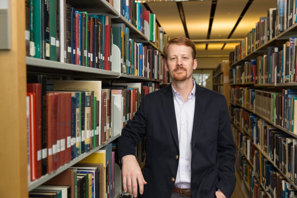 Robert Elder stands beside booksehlves in a library