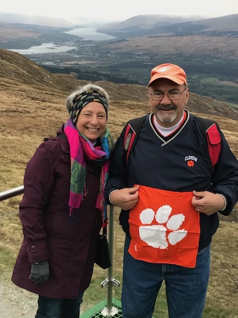 Photo of Lisa and Dave Steele, holding a Clemson Tiger Rag with mountains in the background