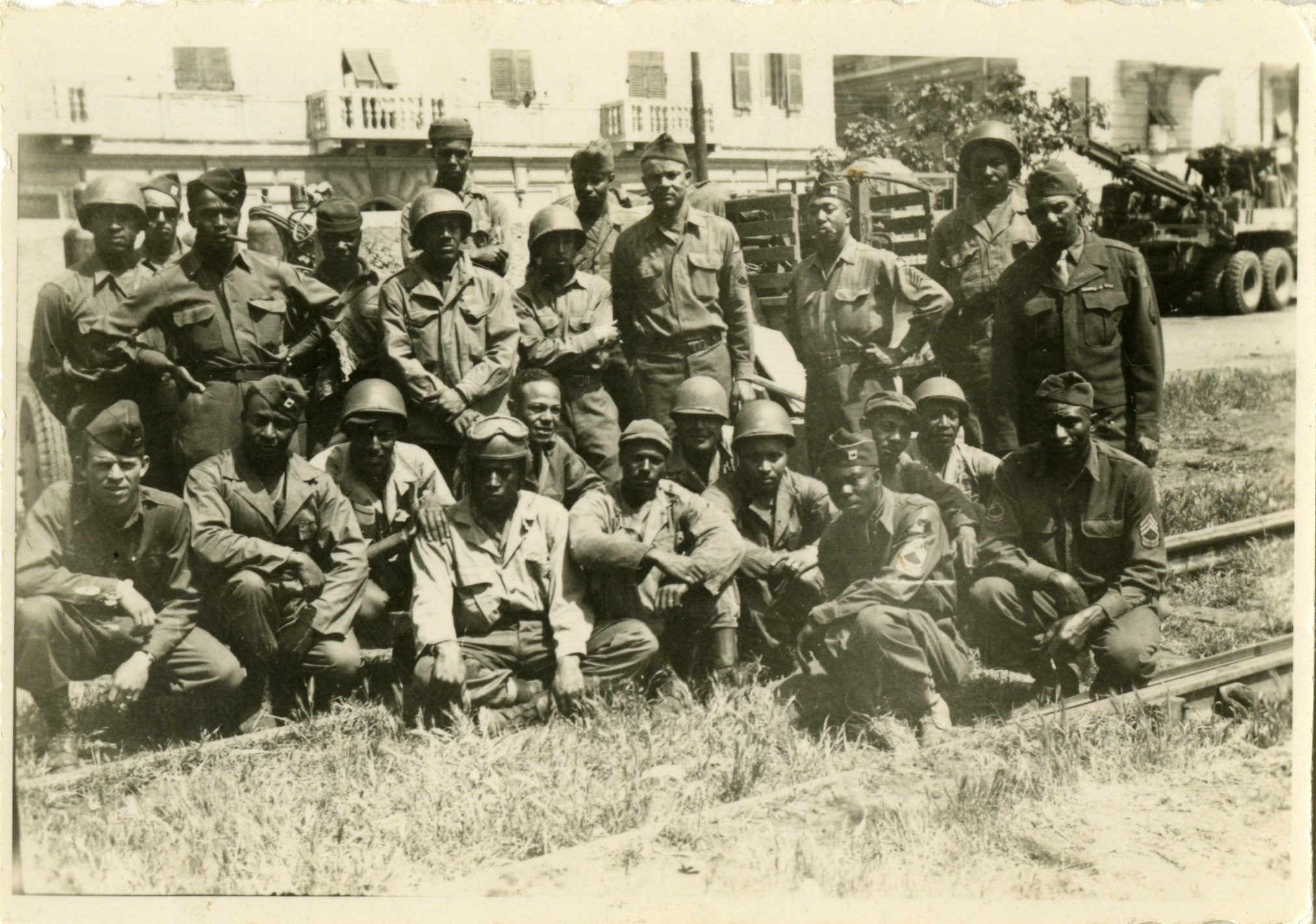 A group of 24 soldiers in front of a building with a tank visible in the background.