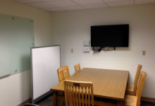 1st floor group study space featuring a table with chairs to seat 4 and a monitor, with a closing door